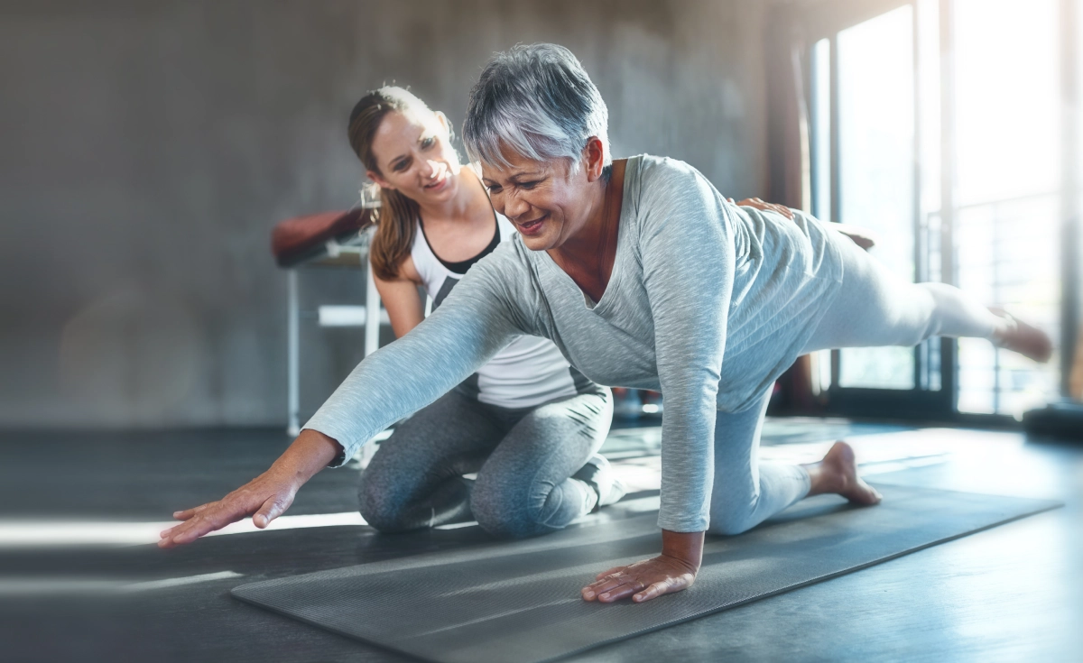 Senior woman doing yoga with trainer.